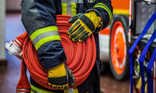 Fireman in action with a rolled fire hose on the emergency vehicle